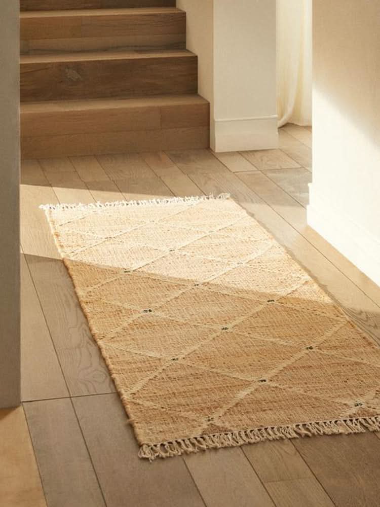 Beige Indian Jute Rug with diamond pattern on wood floor by stairs.